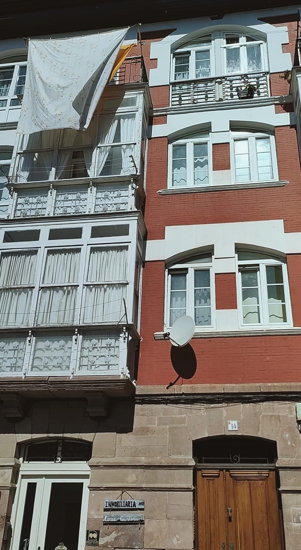 fachada soleada de un edificio antiguo en alguna parte de Cataluña, de ventanas blancas y donde dos sábanas de colores claros se mueven al viento